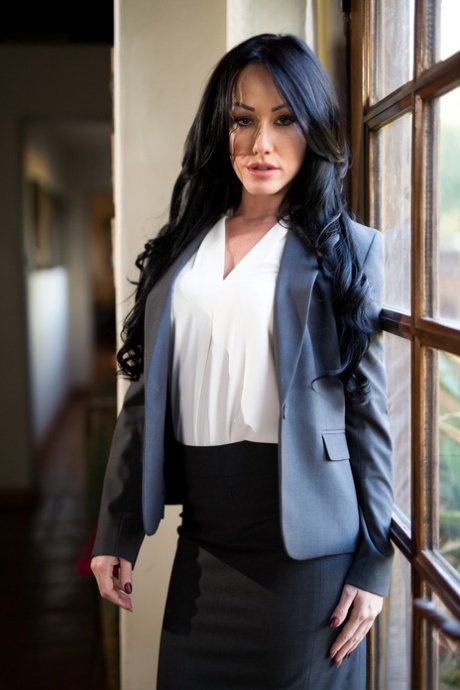 Темноволосая женщина снимает блейзер и юбку, чтобы позировать обнаженной перед окном 1